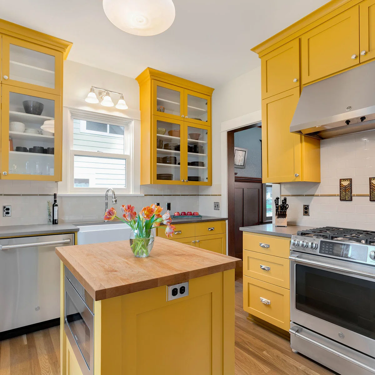 Pale yellow Craftsman kitchen with glass-front upper cabinets and a wood-topped island