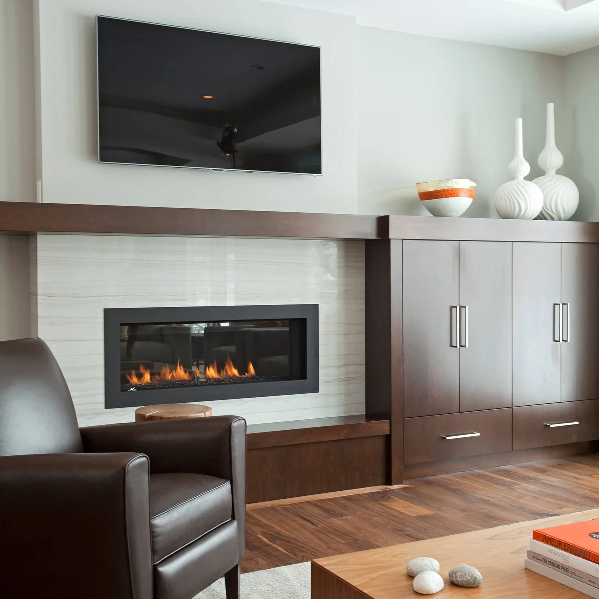 A television above a pale linear fireplace surround with a broad dark wood mantel and matching closed cupboards to the right.