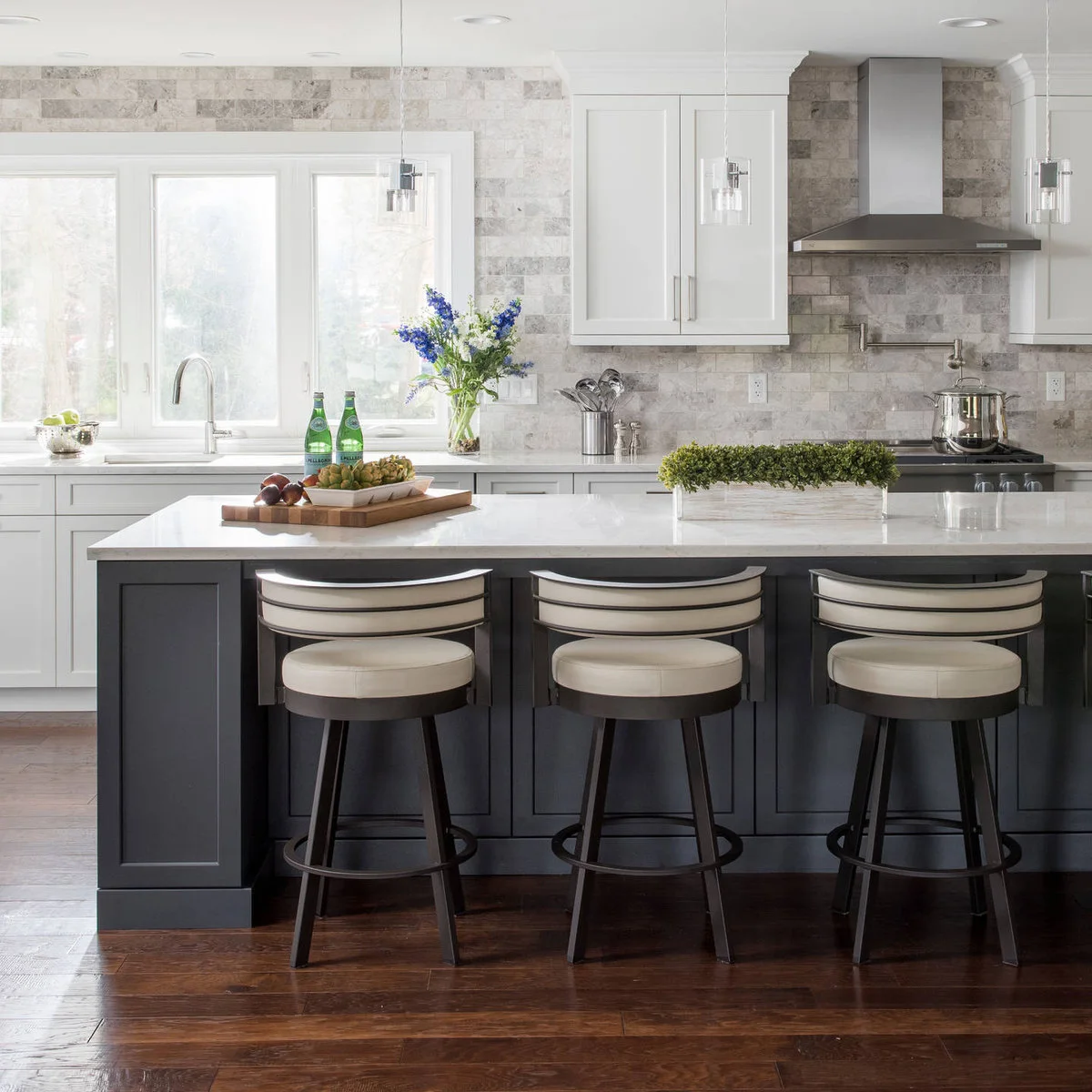 Dark gray paneled kitchen island with a white top and three pale upholstered stools