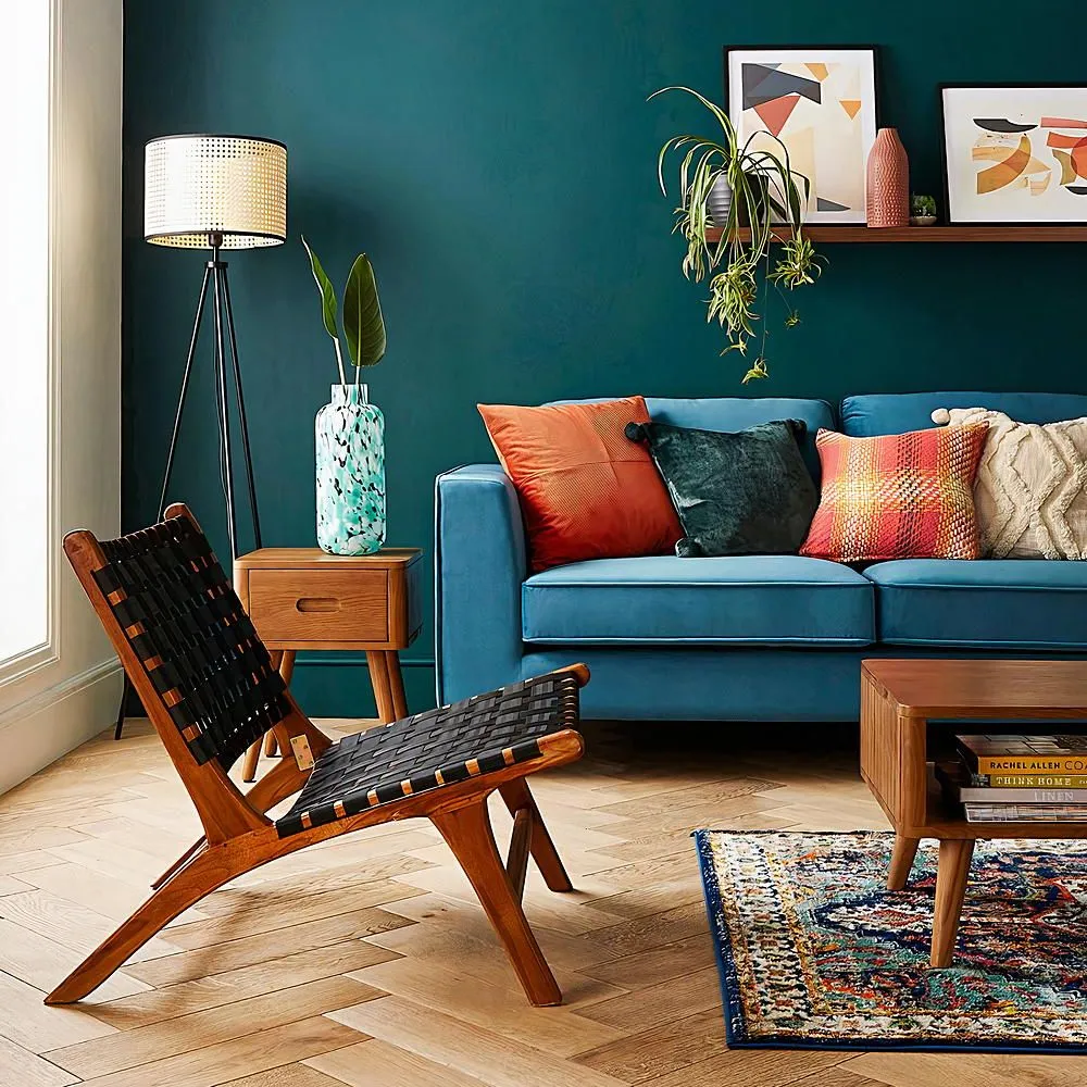 A blue sofa stands beside a timber-framed lounge chair under green walls.