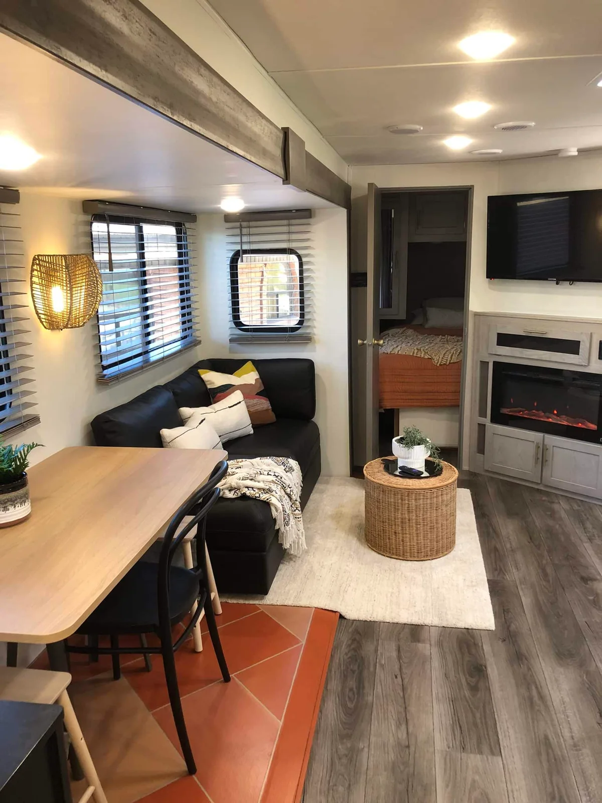 Camper lounge with a wood dining table, black chairs, a dark sofa and a small round woven table.