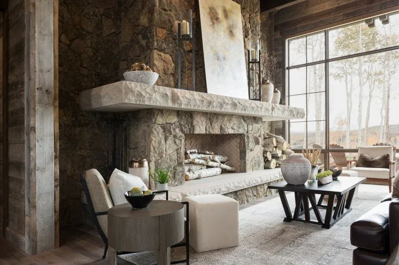 Rustic stone fireplace with broad pale hearth, stored logs and varied tables among light chairs