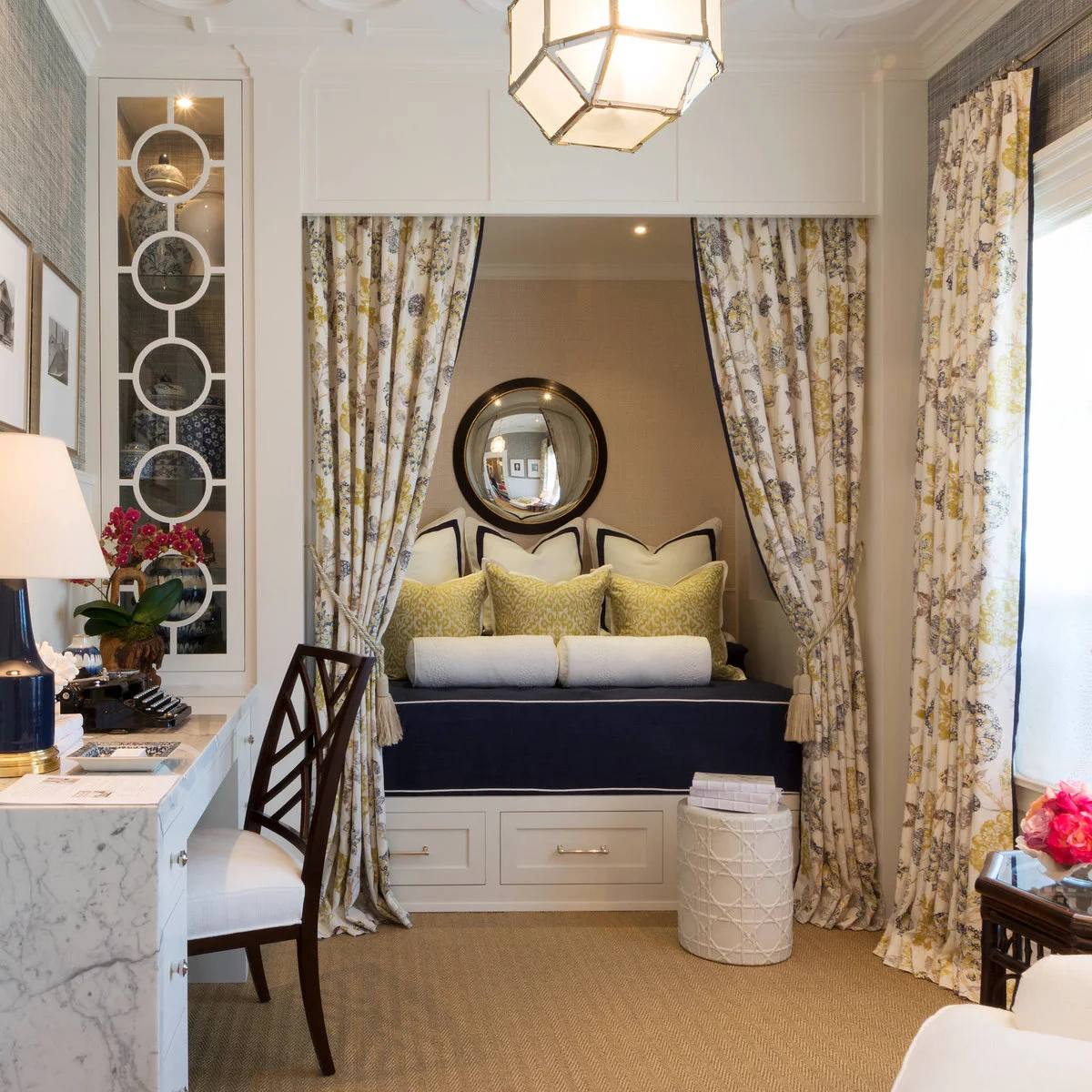 Home office with small writing desk beside a curtained alcove containing a navy upholstered seat and yellow cushions