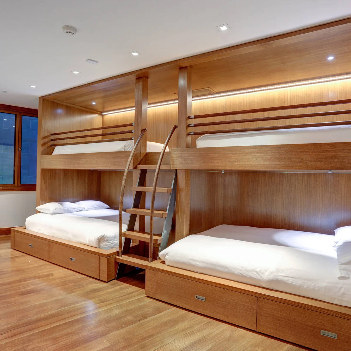 Brown wooden built-in bunks with white bedding, central ladders and drawers beneath the lower beds.