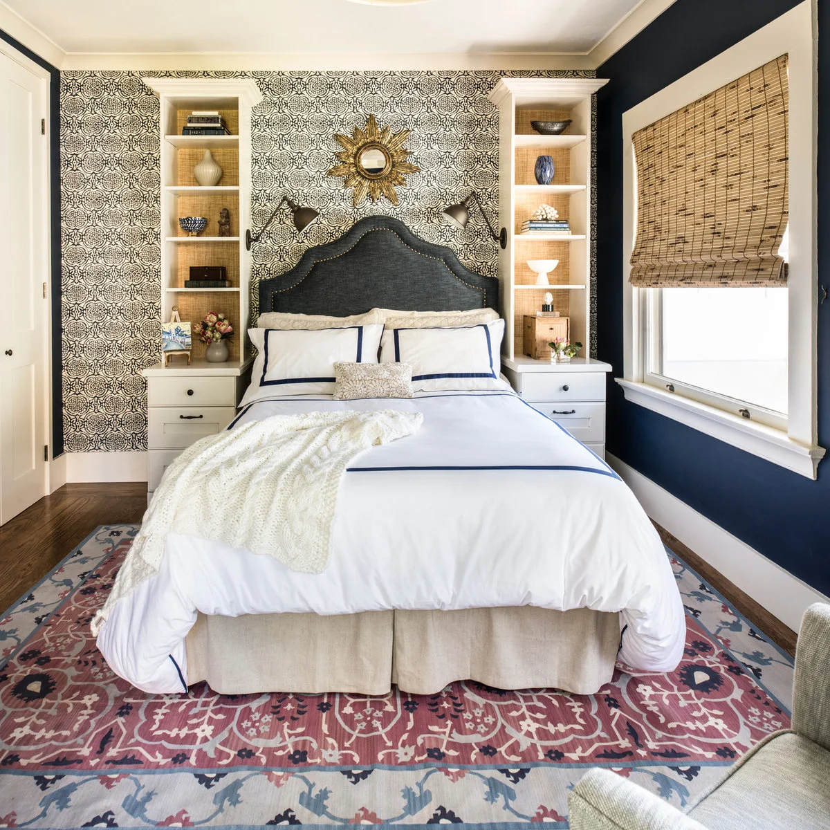 A pink, blue and cream bordered rug extends around a bed between built-in shelves and a navy window wall.