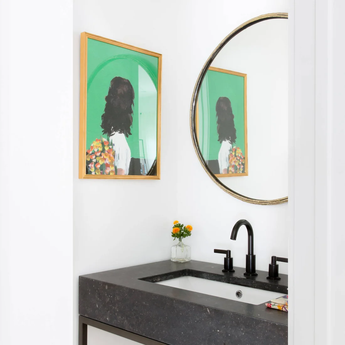Green-background portrait beside a round mirror above a dark bathroom counter