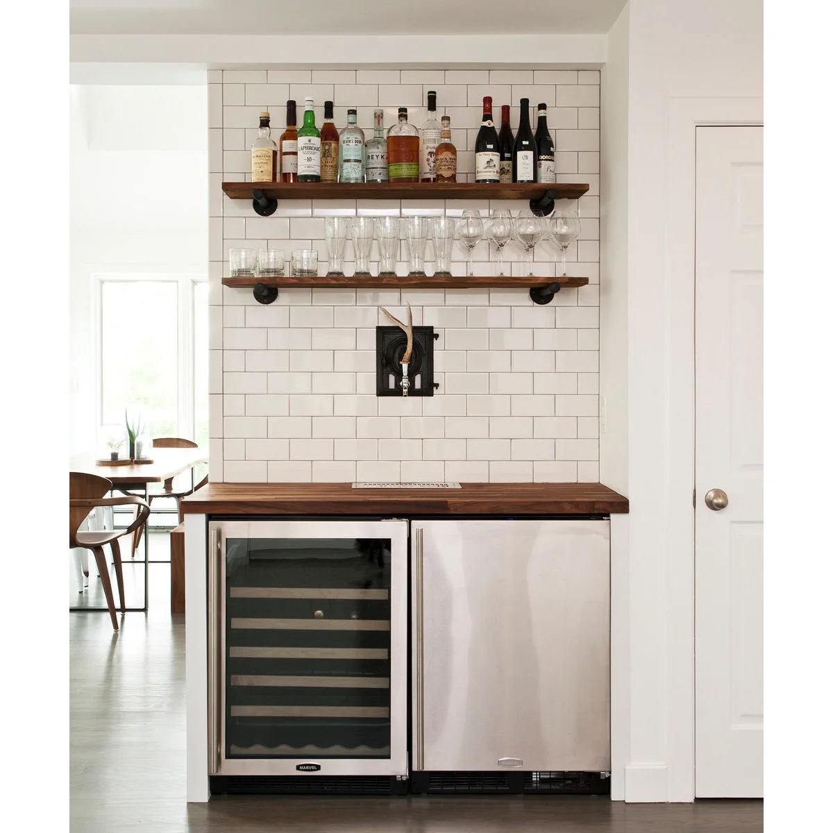 Compact tiled bar with two undercounter appliances, wood shelves, white subway tile and central beverage tap