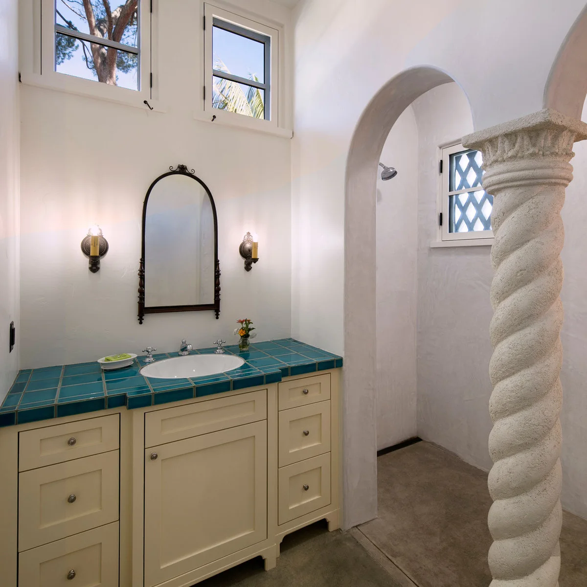 Bathroom with a turquoise square-tiled vanity top, cream cabinet and white arched shower opening
