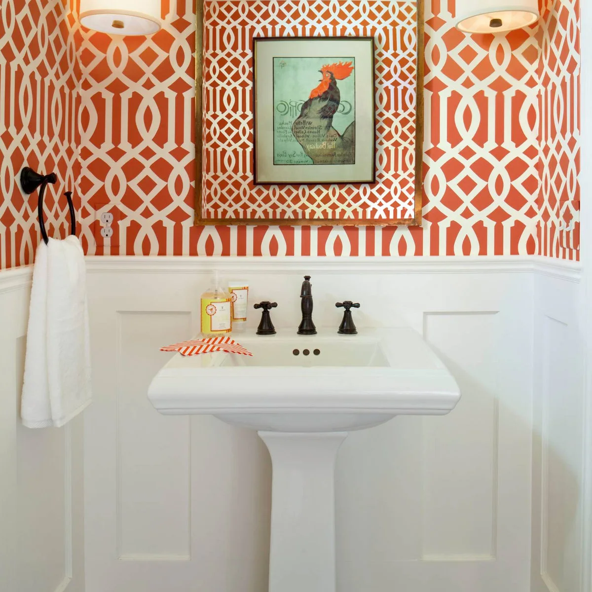 Orange geometric wallpaper above white paneling, with a pedestal sink and dark metal faucet.