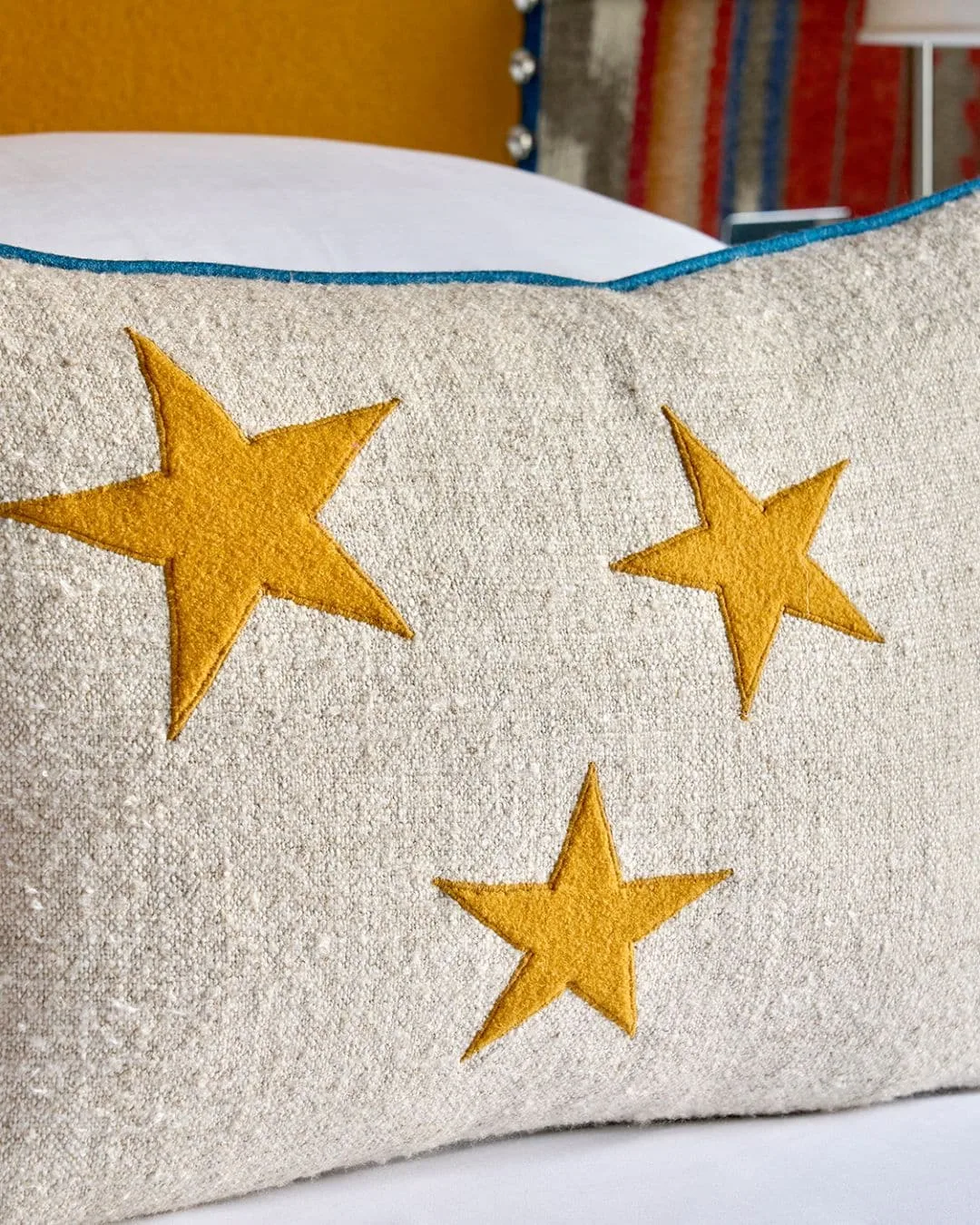 Pale rectangular cushion with three yellow stars and blue edging resting on white bedding.