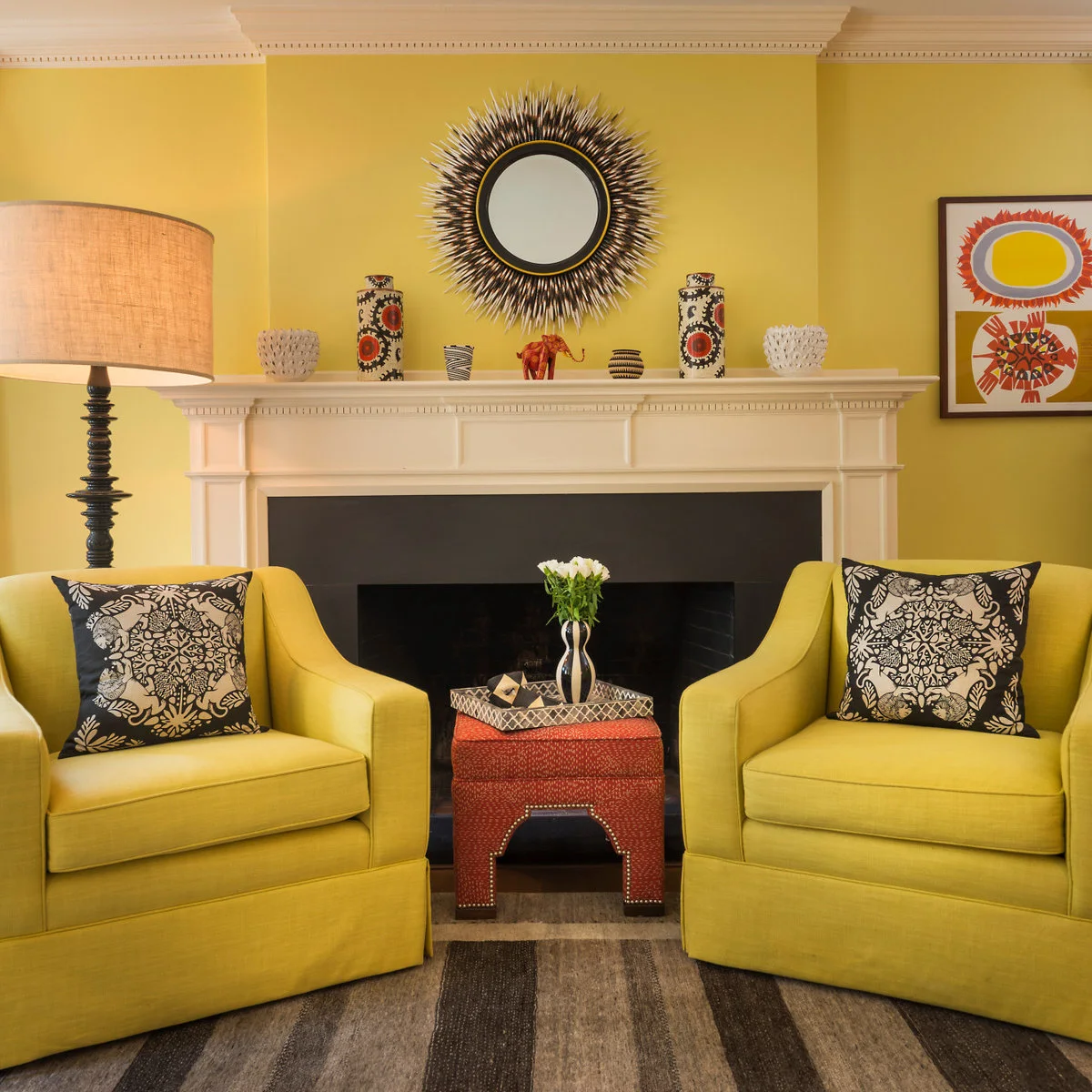 Two yellow armchairs with black-and-white cushions beside a white mantel on a yellow wall