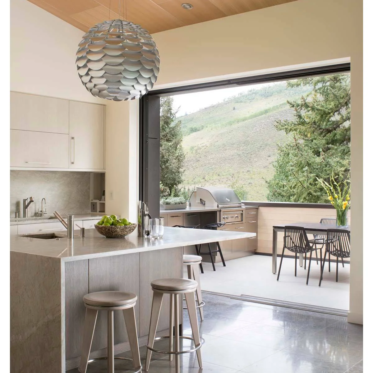 Indoor kitchen opening directly to an outdoor grill counter and dining table through a broad doorway