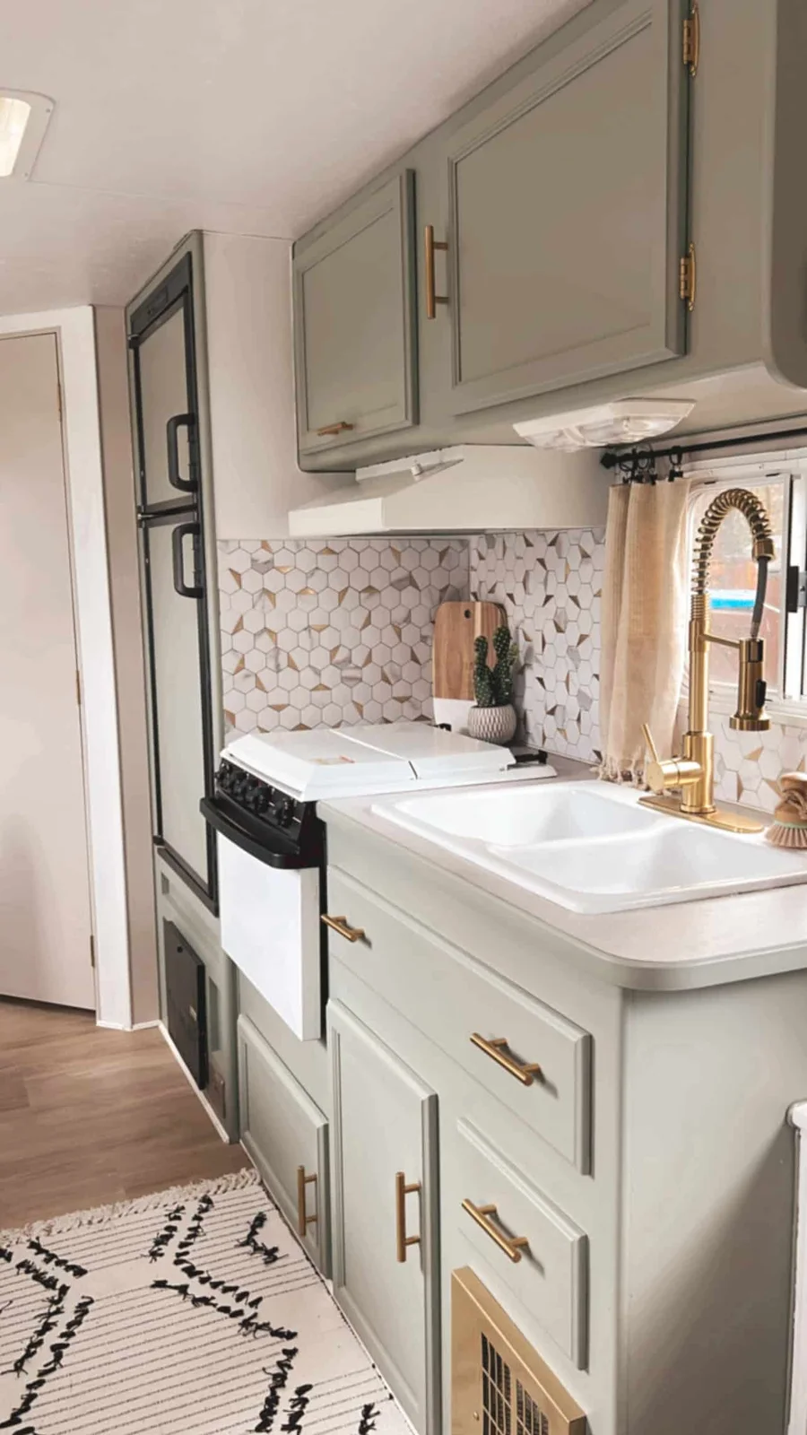 Pale green camper cabinets with gold-colored handles, a matching tall tap and a geometric white backsplash.