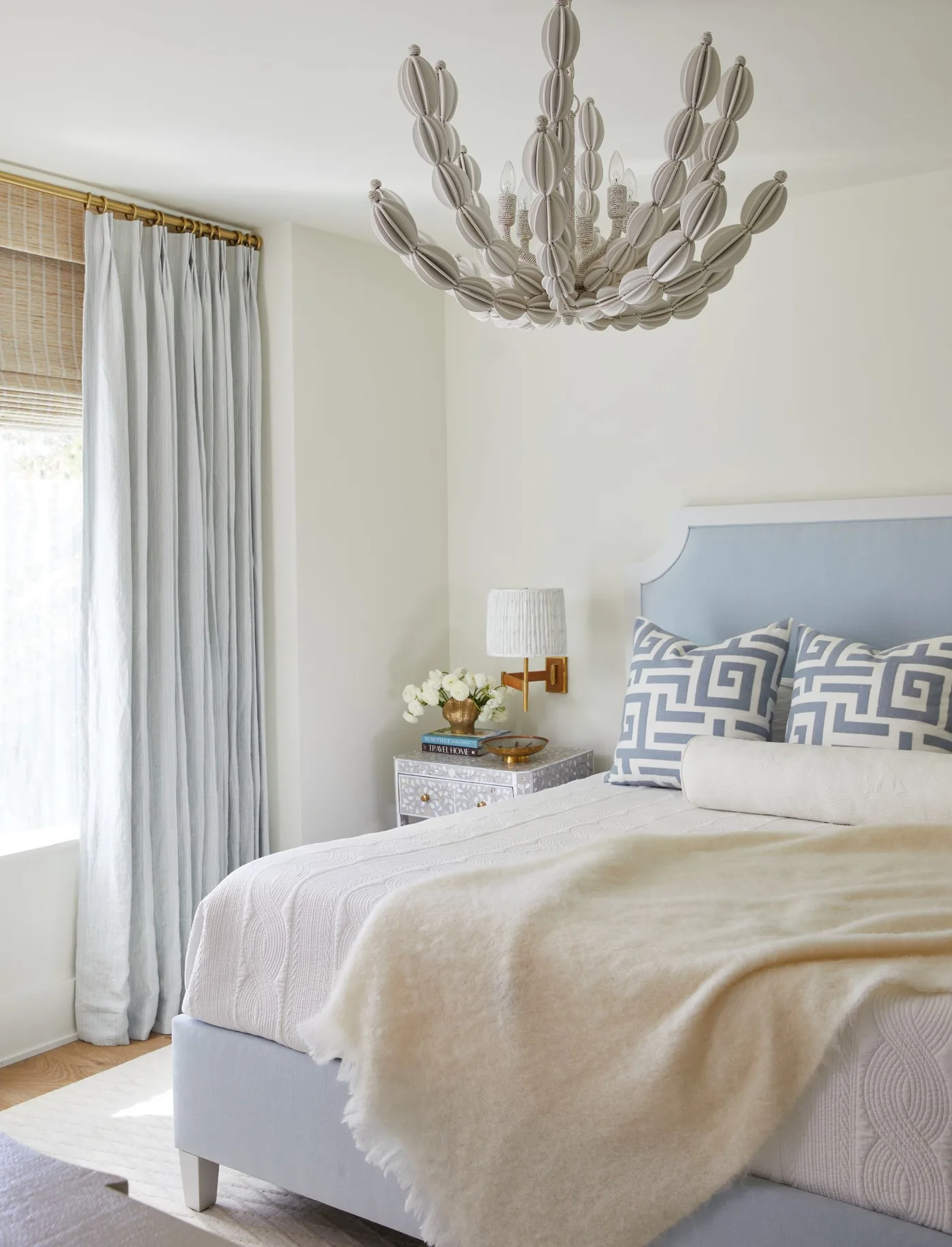 Pale bedroom with a shaped blue upholstered bed, geometric blue cushions, white bedding and a large decorative ceiling light.