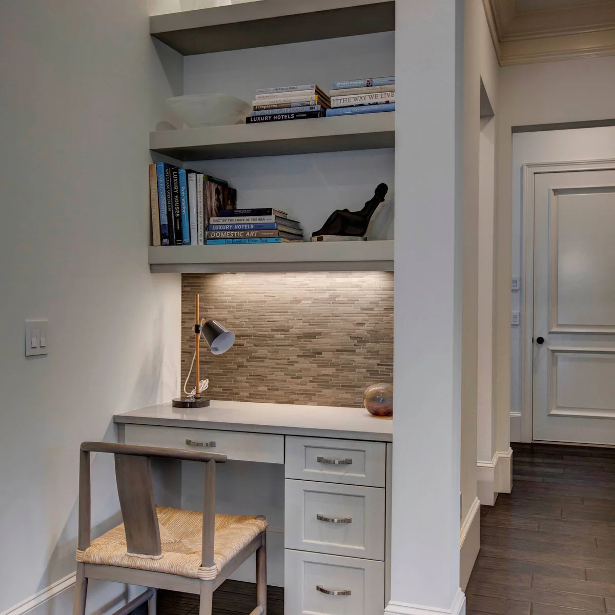 Small gray desk in a recess with right-hand drawers, a wood chair and illuminated shelves above