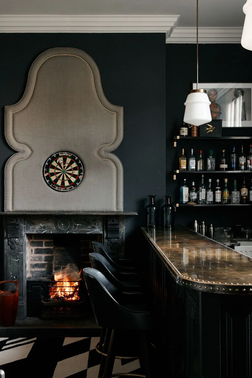 Dark home bar with open bottle shelves, a studded counter edge and a fireplace beside it