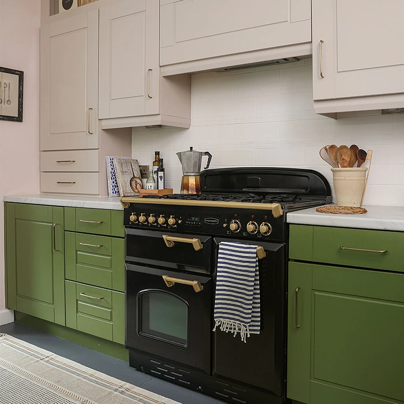Olive green lower cabinets and a black range sit beneath pale pink upper cupboards and a pale tiled wall