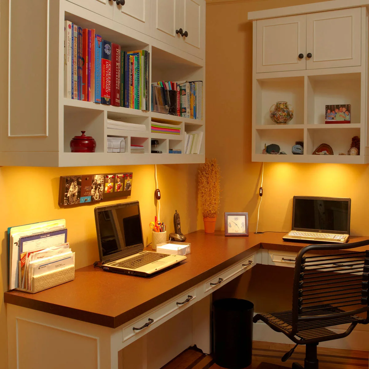 Home office corner with yellow walls, white cabinets, wood-toned worktops and under-cabinet lighting