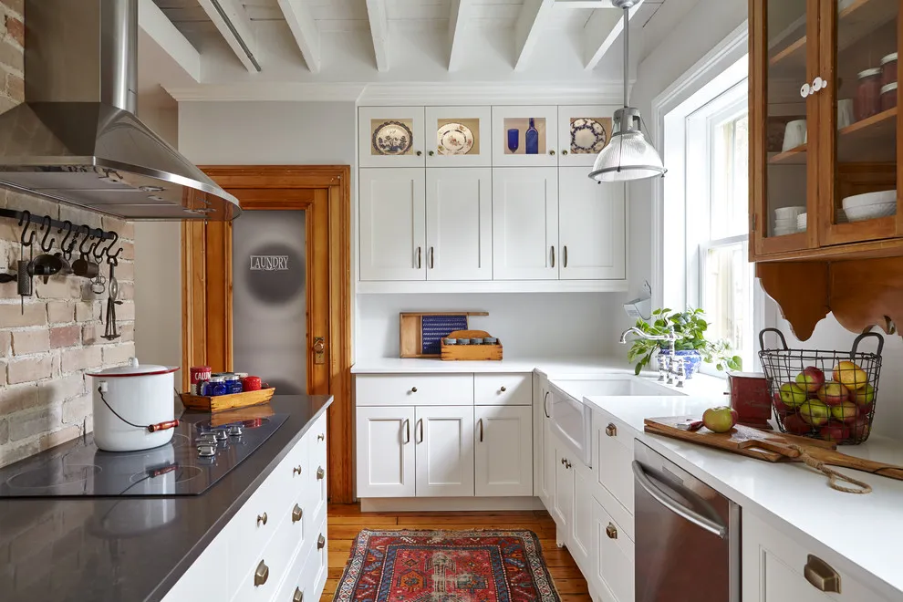 White framed cabinets sit beside warm timber trim, a timber glass-front cupboard and a dark cooktop below a metal hood.