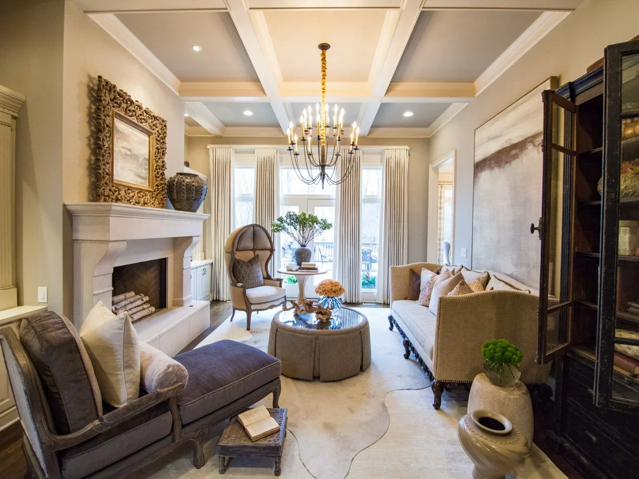 A neutral sofa, dark upholstered bench and rounded high-back chair surround a round ottoman in a formal sitting room.