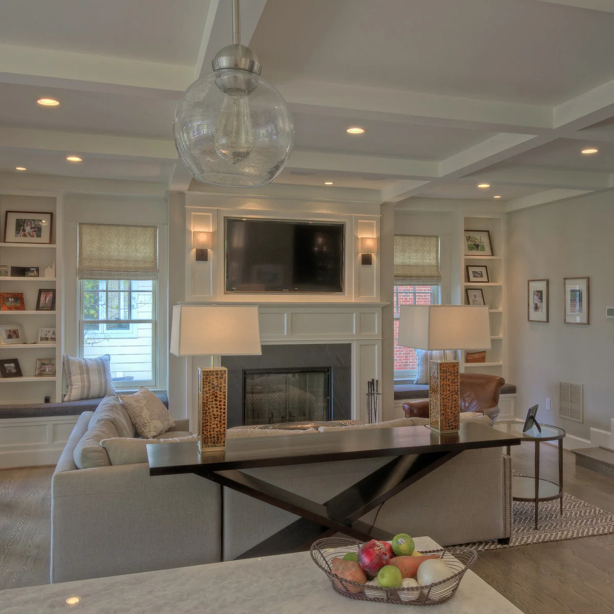 A sofa-back console with two tall lamps facing a white fireplace wall, television, side windows and built-in window seats.