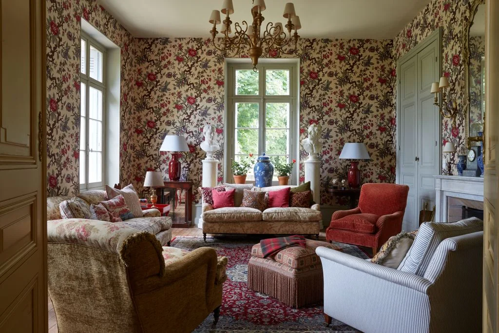 Traditional sitting room with floral wallcovering, patterned sofas, a red armchair and pale blue trim