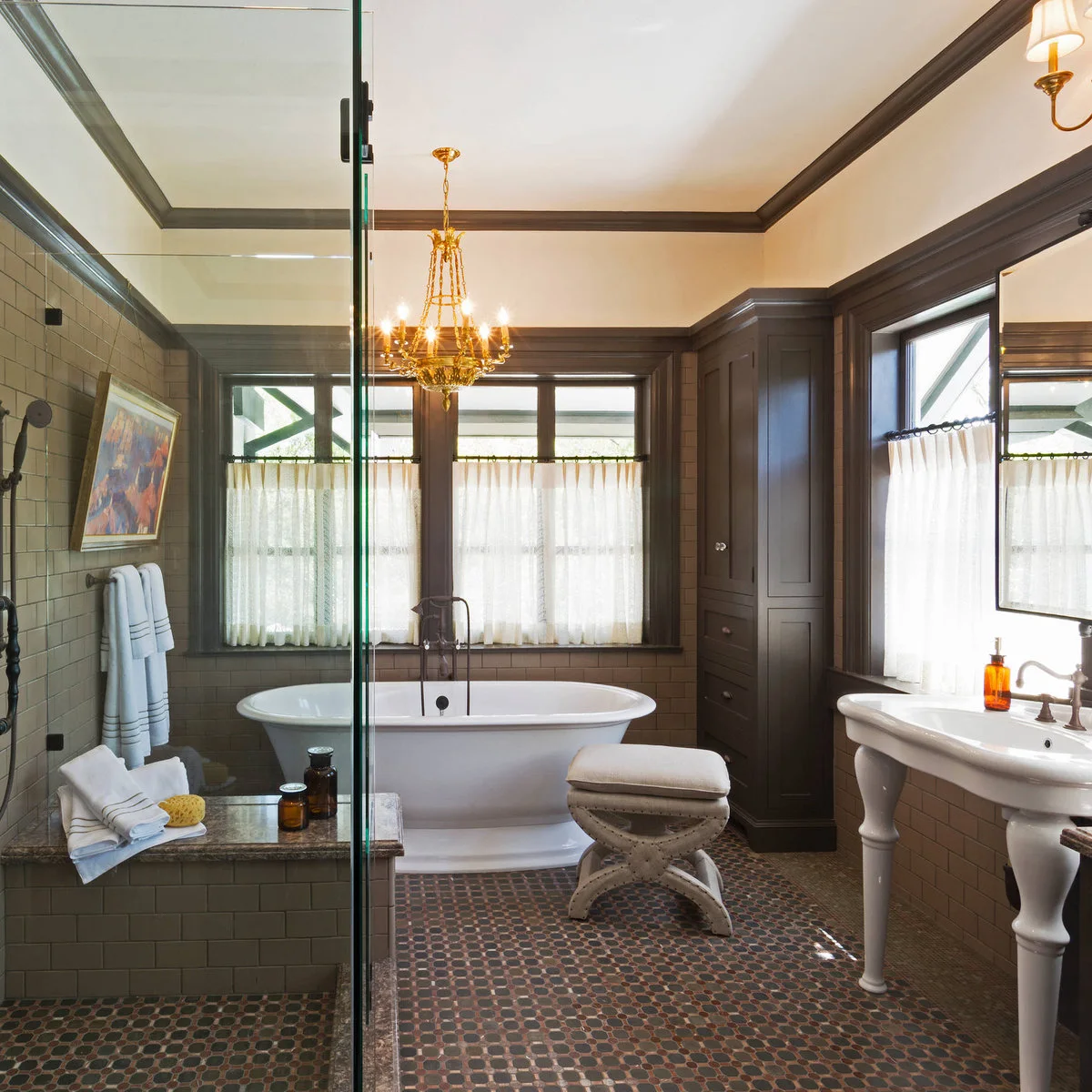 Pale cafe curtains cover lower window panes around a white tub in a bathroom with dark trim and muted green tile.