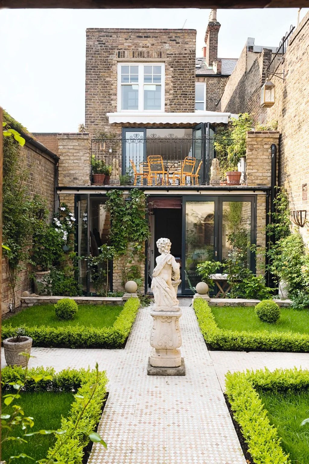 A tiled cross path separates low hedges and lawn within a walled garden