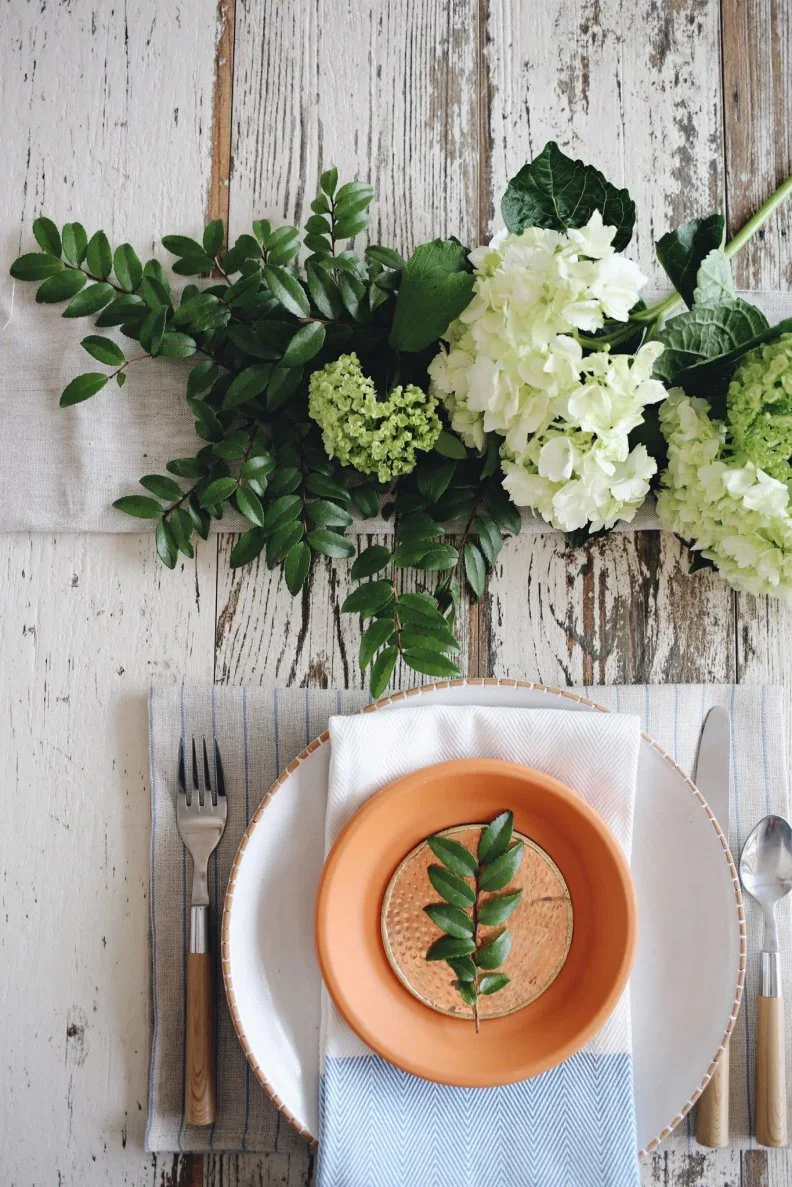 A green sprig rests on a small orange textured plate above a white napkin and pale dinner plate