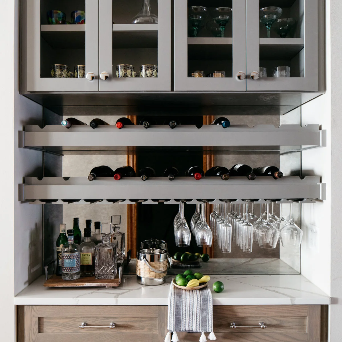 Mini bar with horizontal bottle rails, hanging stemware, mirrored backing and a light counter above wood drawers