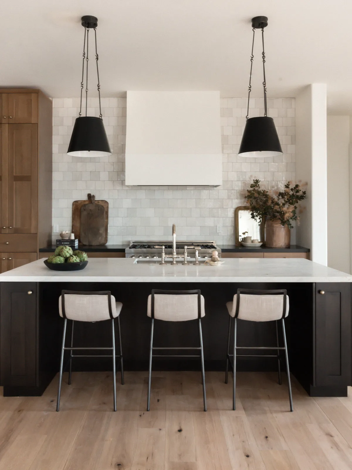A black island stands between pale timber cabinets beneath simple dark pendants.