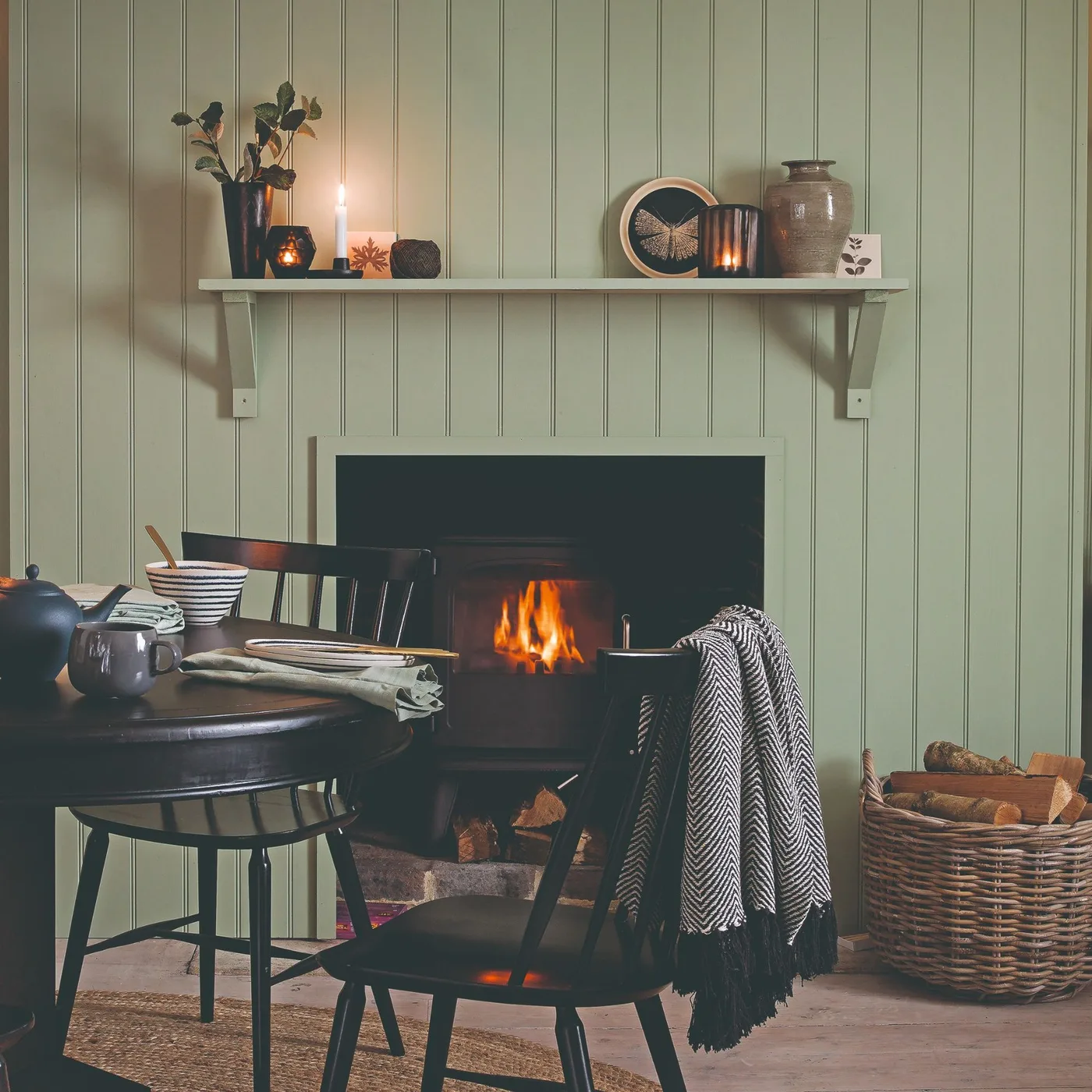 Sage paneled fireplace with dark stove, woven log basket and black dining furniture