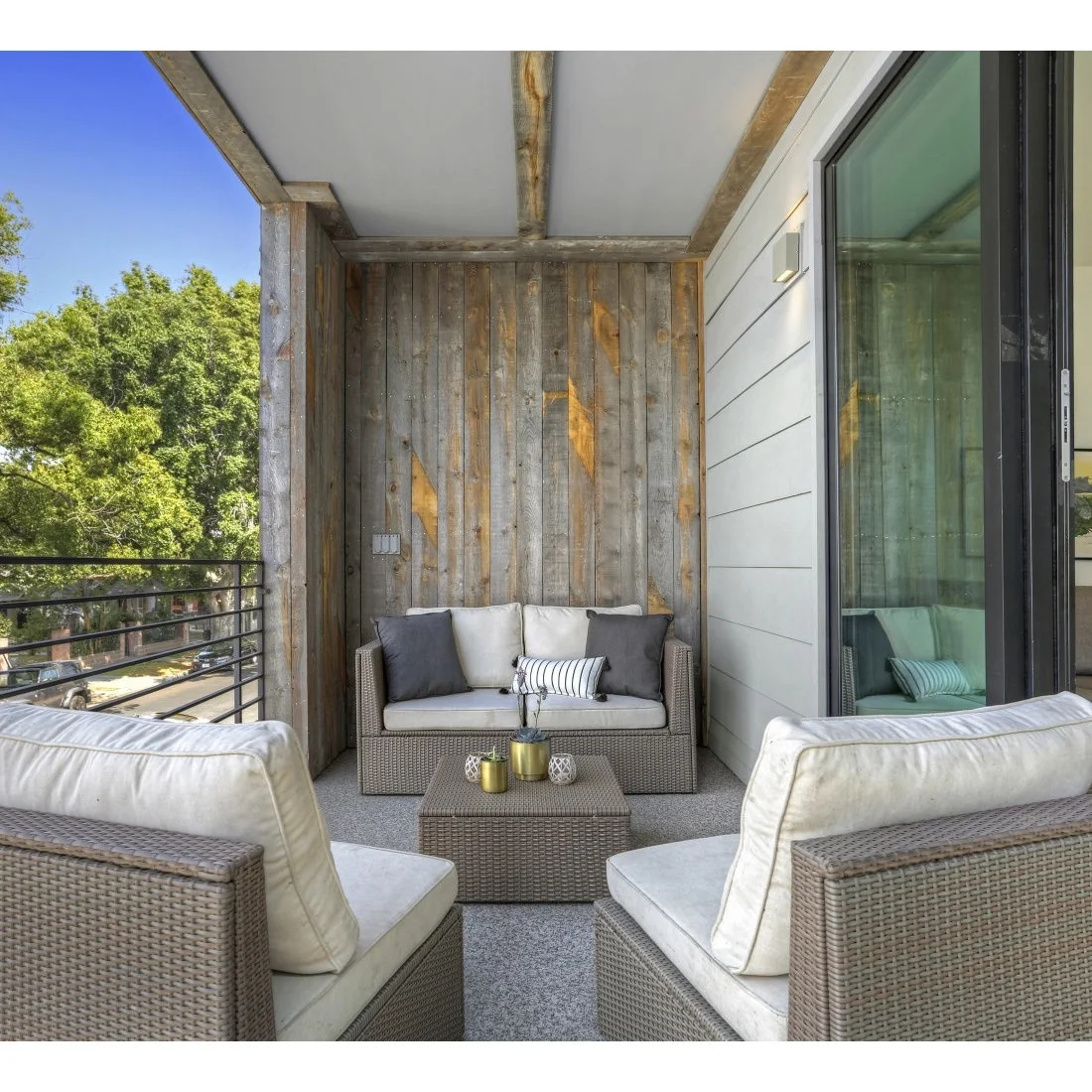 A compact woven table sits between pale cushioned chairs and a loveseat on a covered balcony