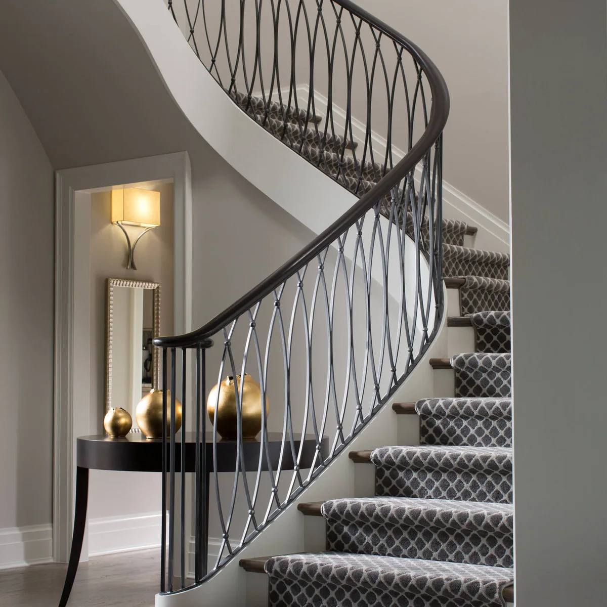 Curved staircase with a grey linked-pattern runner and dark diamond-detail railing