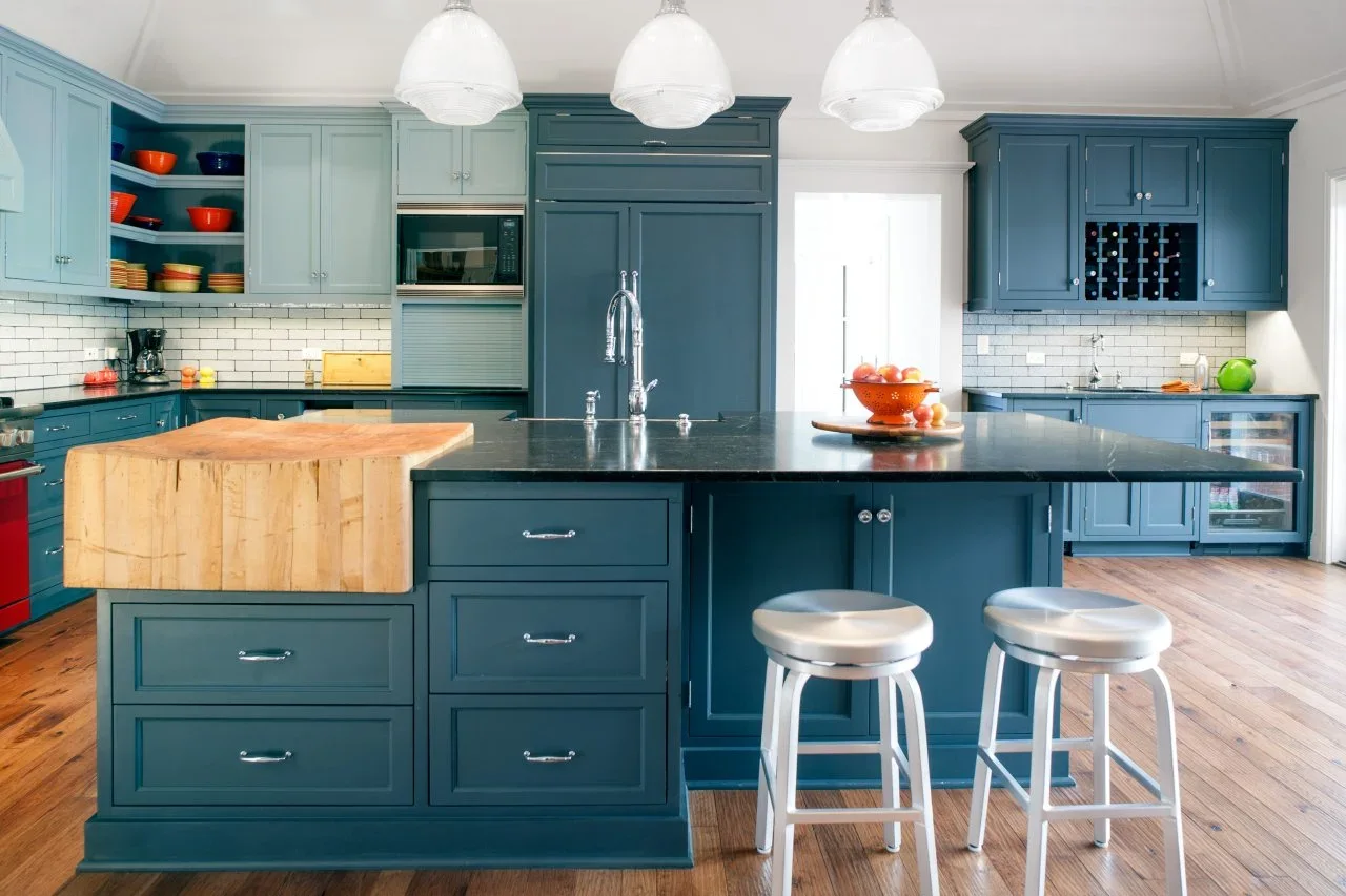Pale blue upper cabinets contrast with deeper blue lower and tall cupboards around a dark-topped island and raised wood chopping block.