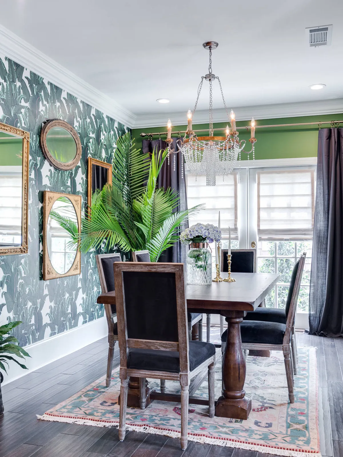 Green foliage wallpaper surrounds a timber dining table and dark chairs.