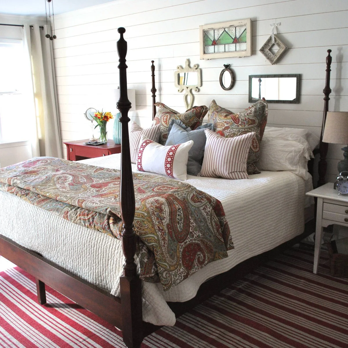 Dark four-poster bed with white bedding, paisley accents and small mirrors on a pale plank wall