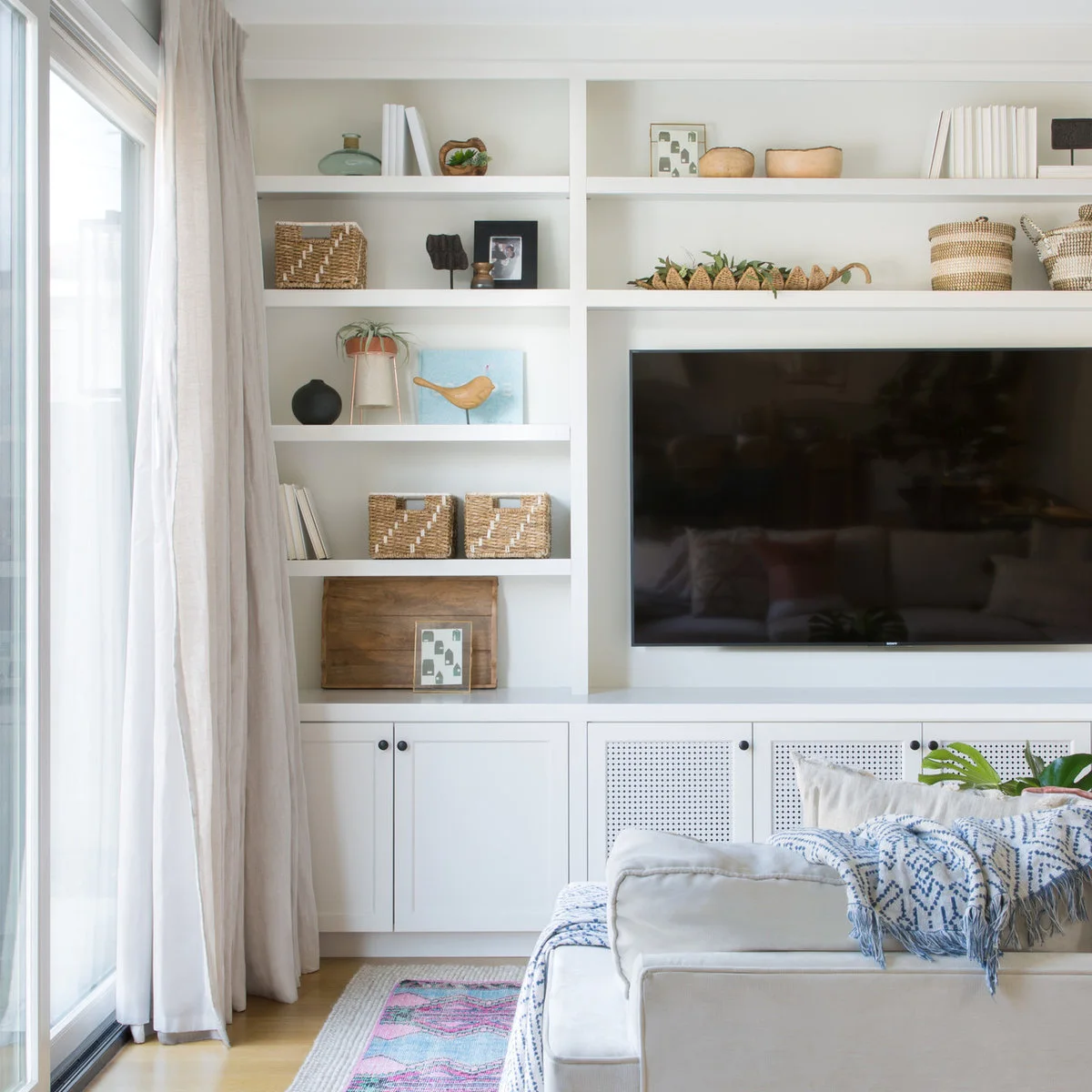 White built-in shelves beside a television display woven baskets, small art and vessels above lower cabinet doors with perforated panels.