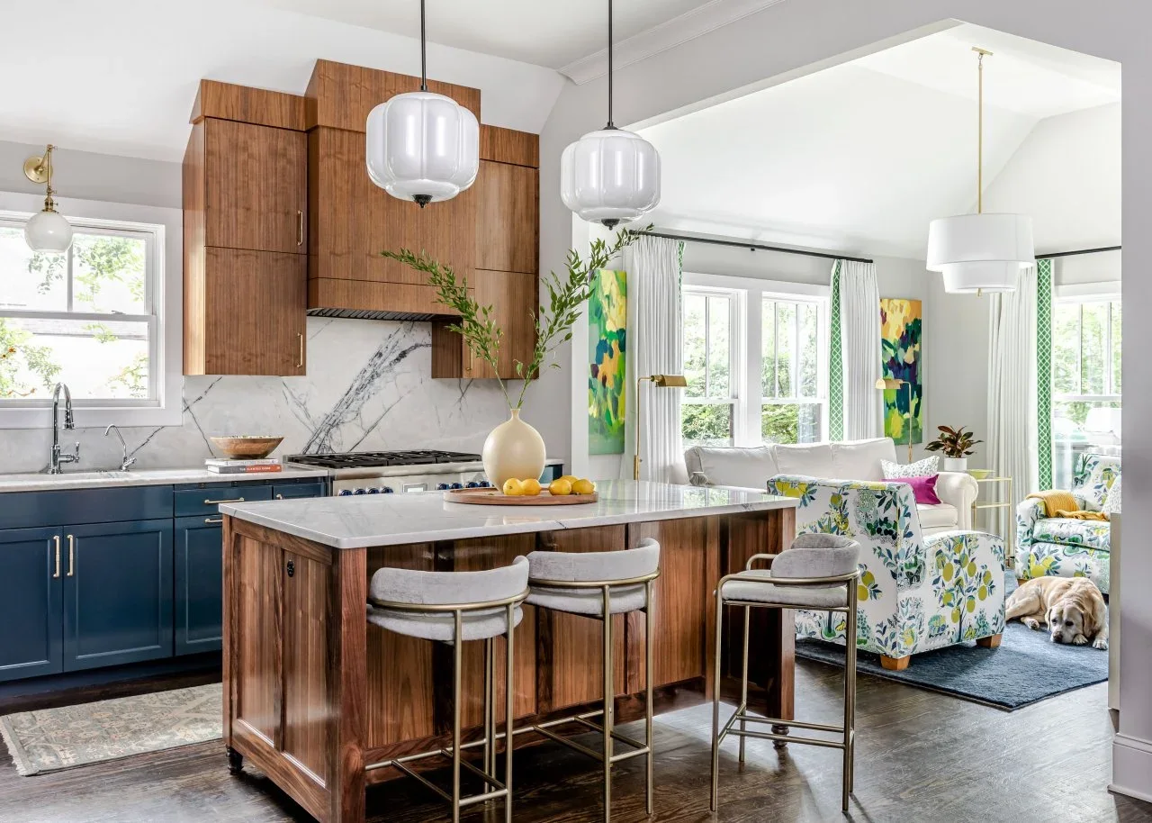 Rich wood upper cabinets, a matching hood surround and an island contrast with deep blue lower cupboards beside a sitting area.