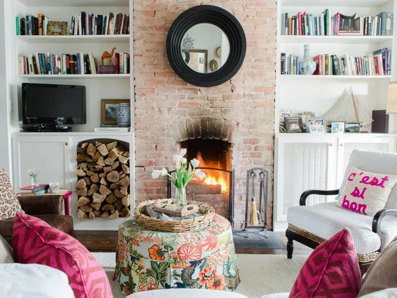 White fitted shelves beside exposed brick fireplace with television, lower log compartment and pink accents
