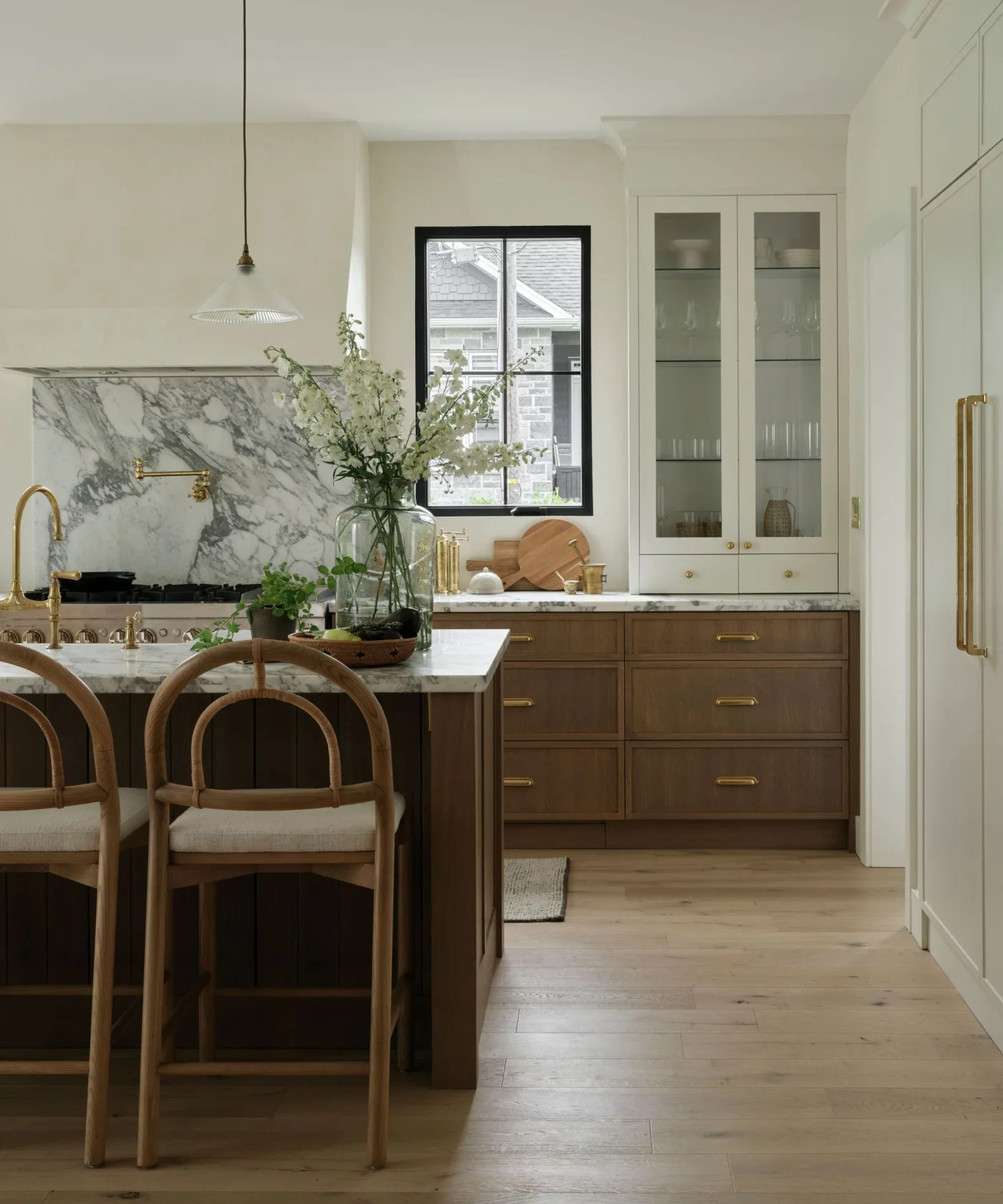 Kitchen with glass-front upper cabinets, wooden lower drawers and a pale backsplash with sweeping gray veins behind the cooktop.
