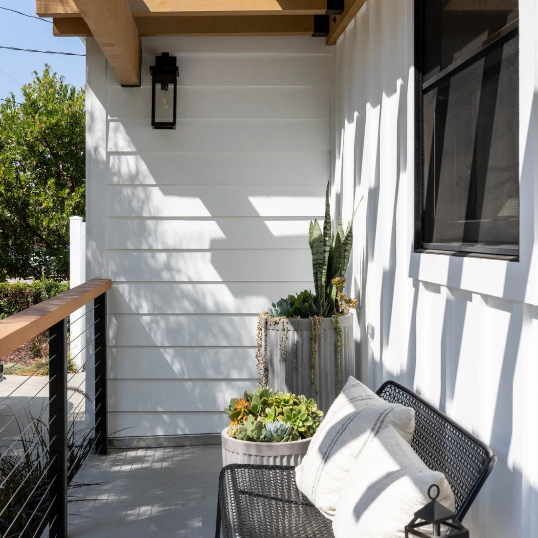 A black woven chair sits beside tall and low pale planters filled with upright and trailing greenery