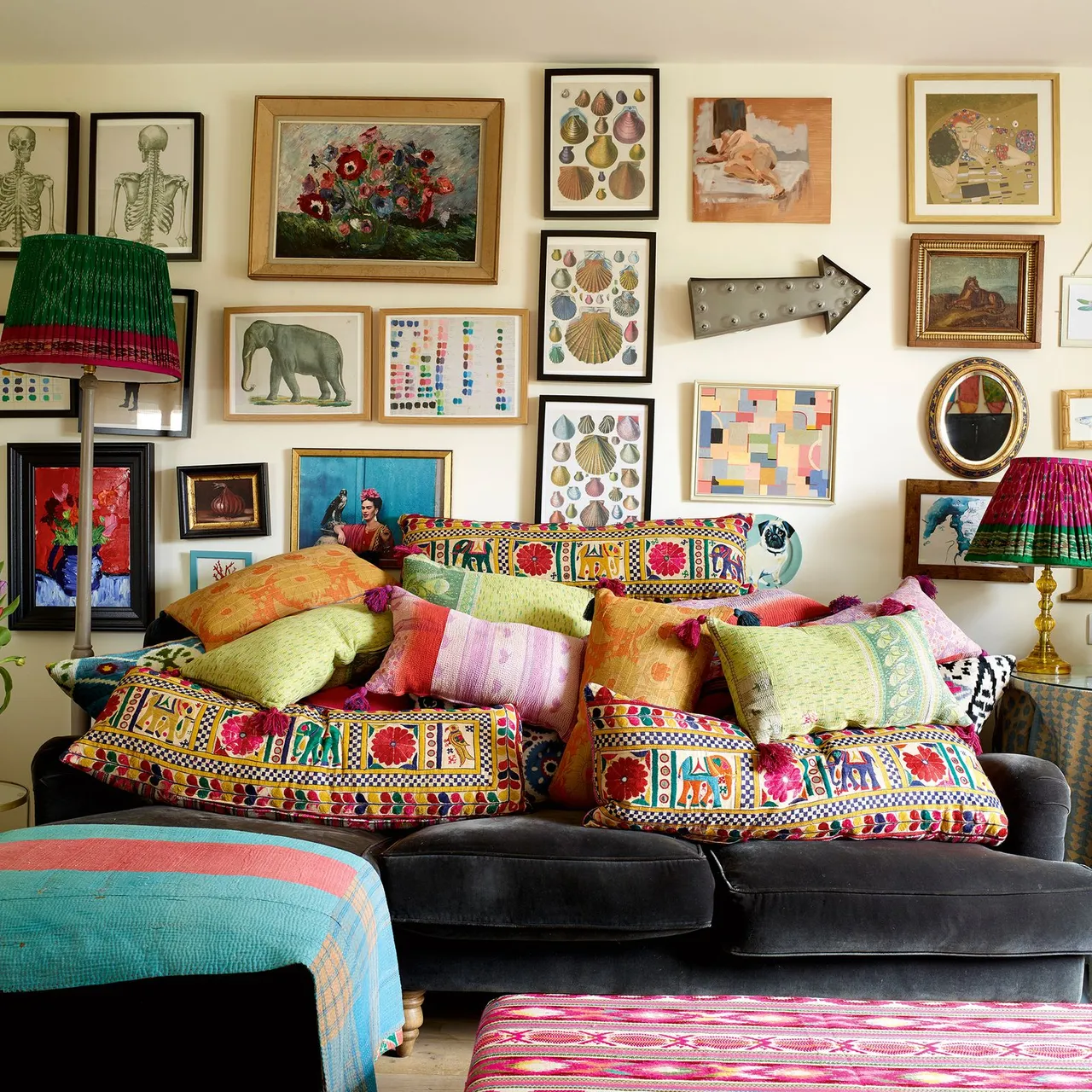 Numerous framed pictures rise above a sofa filled with colorful cushions.
