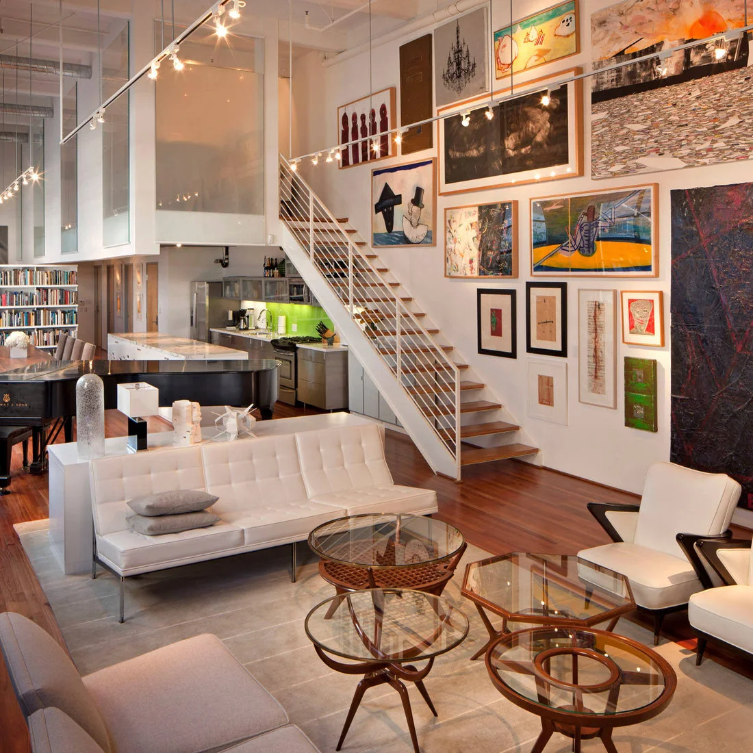White seating around glass topped tables beneath a large gallery wall and open stair