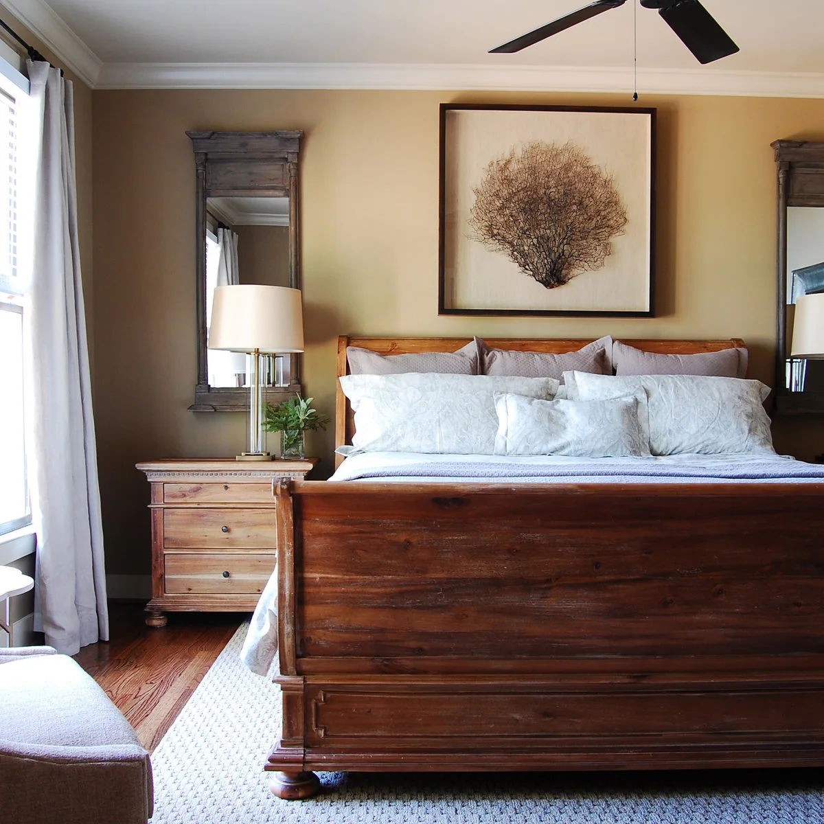 A wooden sleigh bed with pale bedding, wooden bedside drawers, tall mirrors and shaded lamps.
