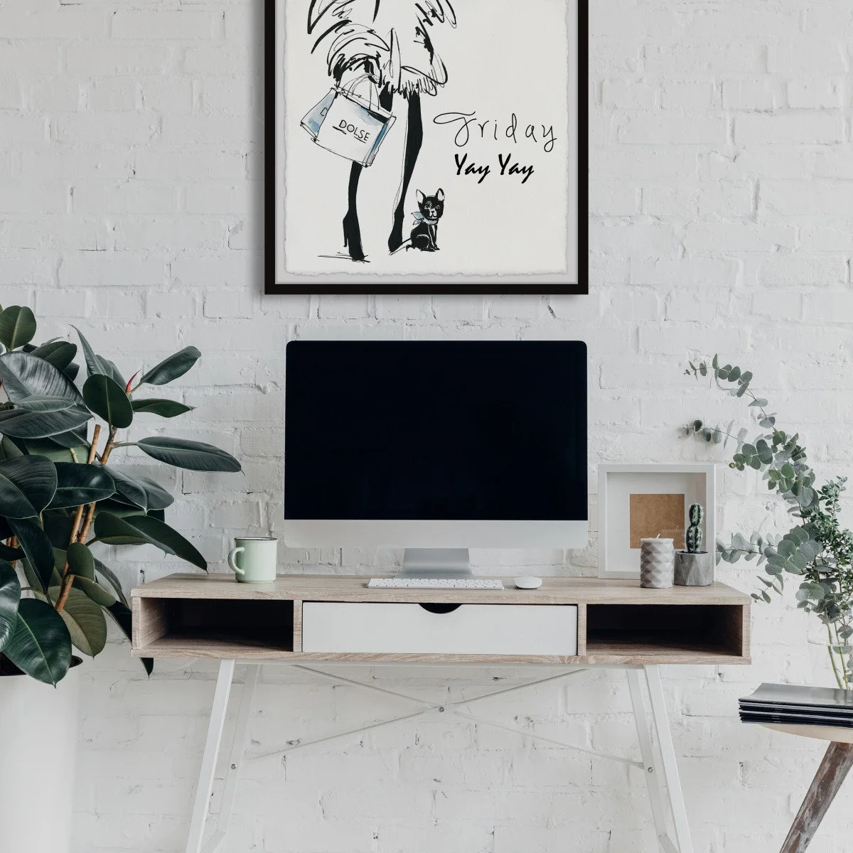 Small wood-and-white desk against a white brick wall with desktop computer, large leafy plant and framed artwork