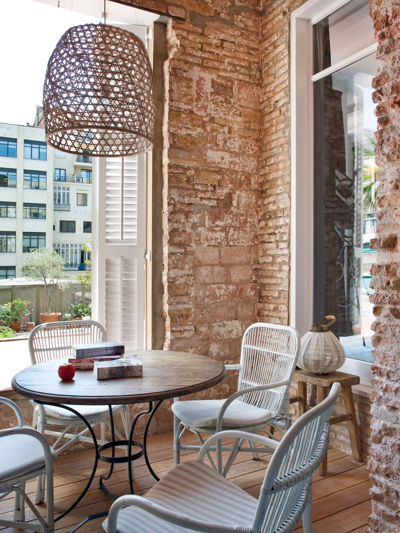 Open woven pendant above a round dark table with pale woven chairs beside exposed brick walls