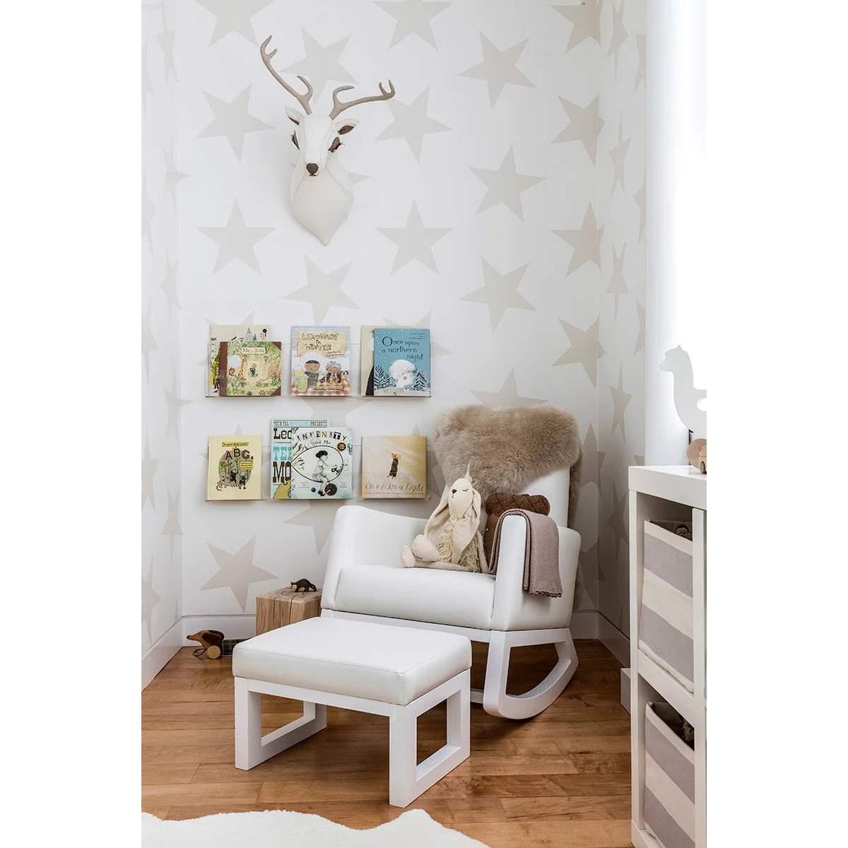 White nursery rocking chair and matching footstool beneath star wallpaper beside shallow book ledges