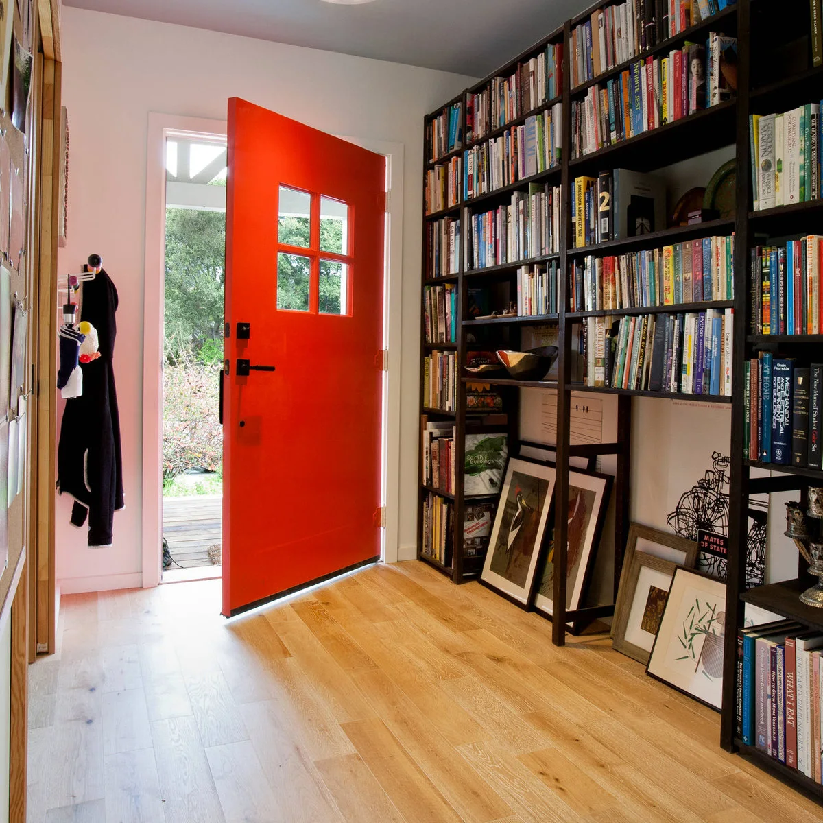 Small entrance with an orange-red front door, light wood floor and a wall of dark bookshelves.