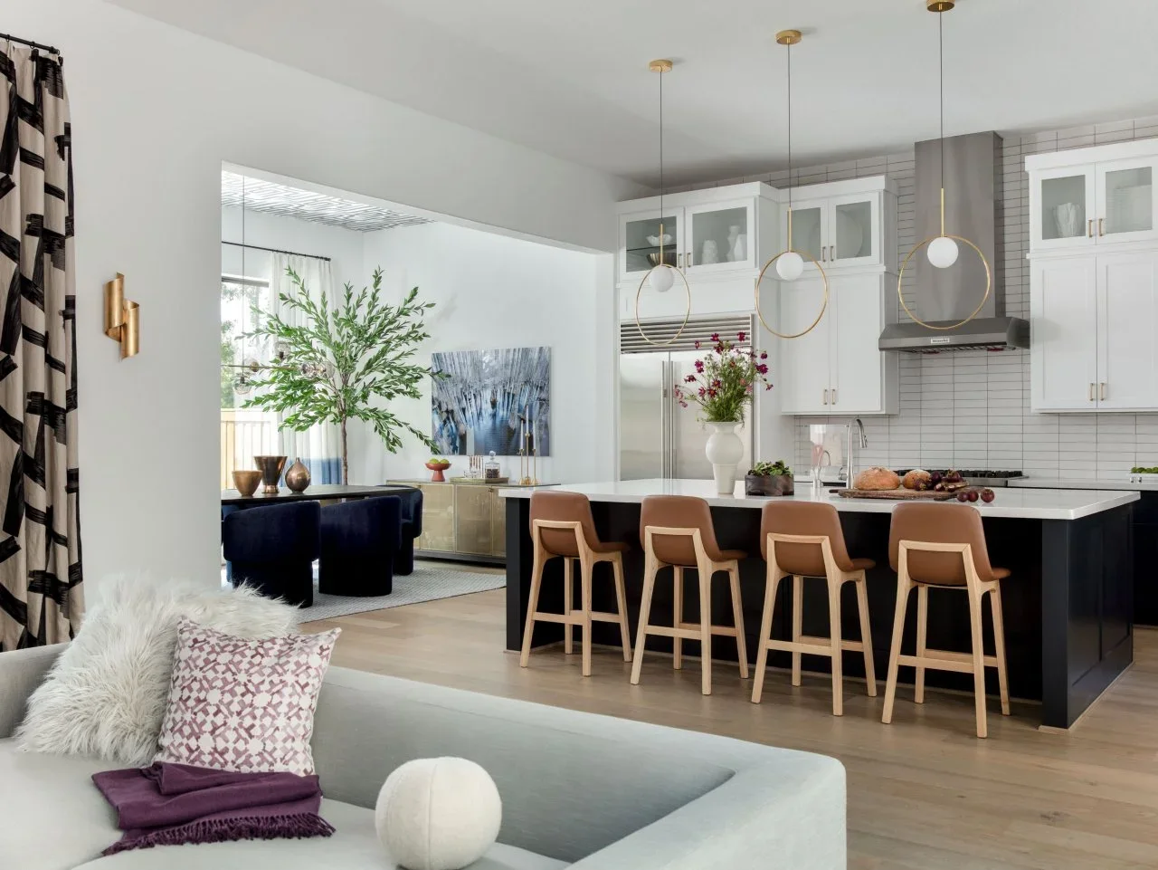 A dark kitchen island with tan stools sits between a pale sofa and an adjoining dining area with dark blue chairs.